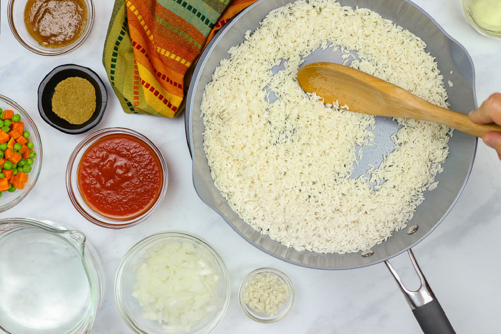 Rice in a skillet with ingredients for Restaurant Style Mexican Rice next to it