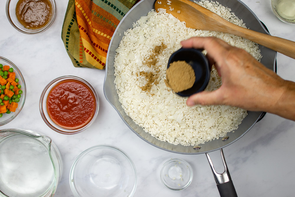 Diced onions, cumin, and rice in a skillet with ingredients for Restaurant Style Mexican Rice next to it