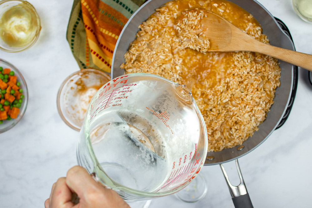 In-process Restaurant Style Mexican Rice in a skillet, with all ingredients except peas and carrots