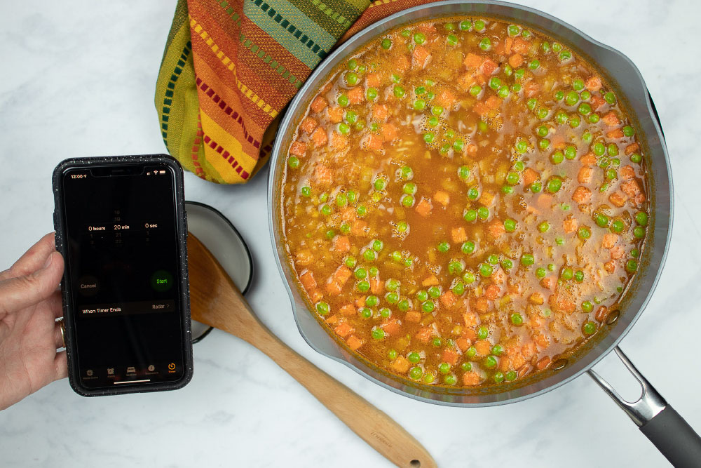In-process Restaurant Style Mexican Rice in a skillet, and a hand holding a phone using the timer