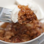 A fork picking up a bite of Apple Crumble topped with ice cream.