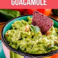 Homemade guacamole in a rainbow-striped bowl, with half an avocado in the background.