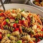Colorful rotini pasta in a bowl with diced peppers and nuts