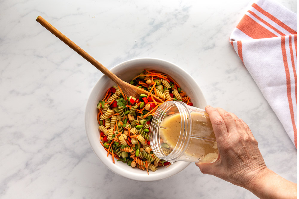 pouring sesame-ginger dressing over Thai pasta Salad.