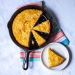Sliced cornbread in a round cast iron skillet and piece of cornbread on a plate
