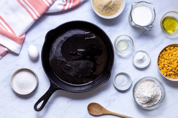 cast iron skillet with oil and ingredients for cornbread with corn kernels