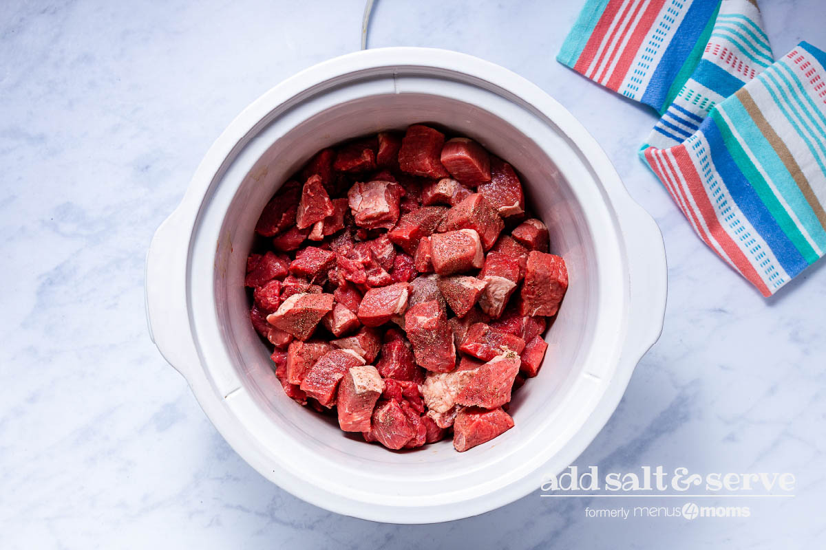 Overhead view of beef in a crock pot for Carne Guisada.