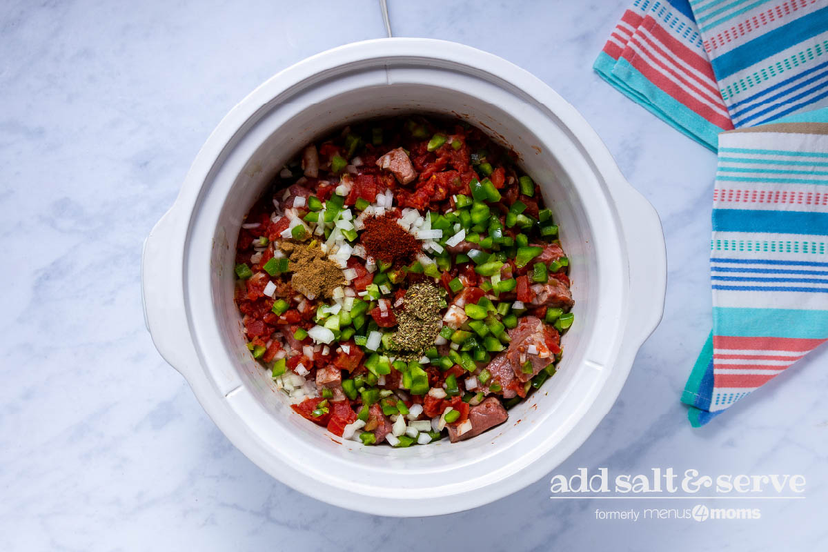 Overhead view of meat, vegetables, and spices for Carne Guisada in a crock pot.