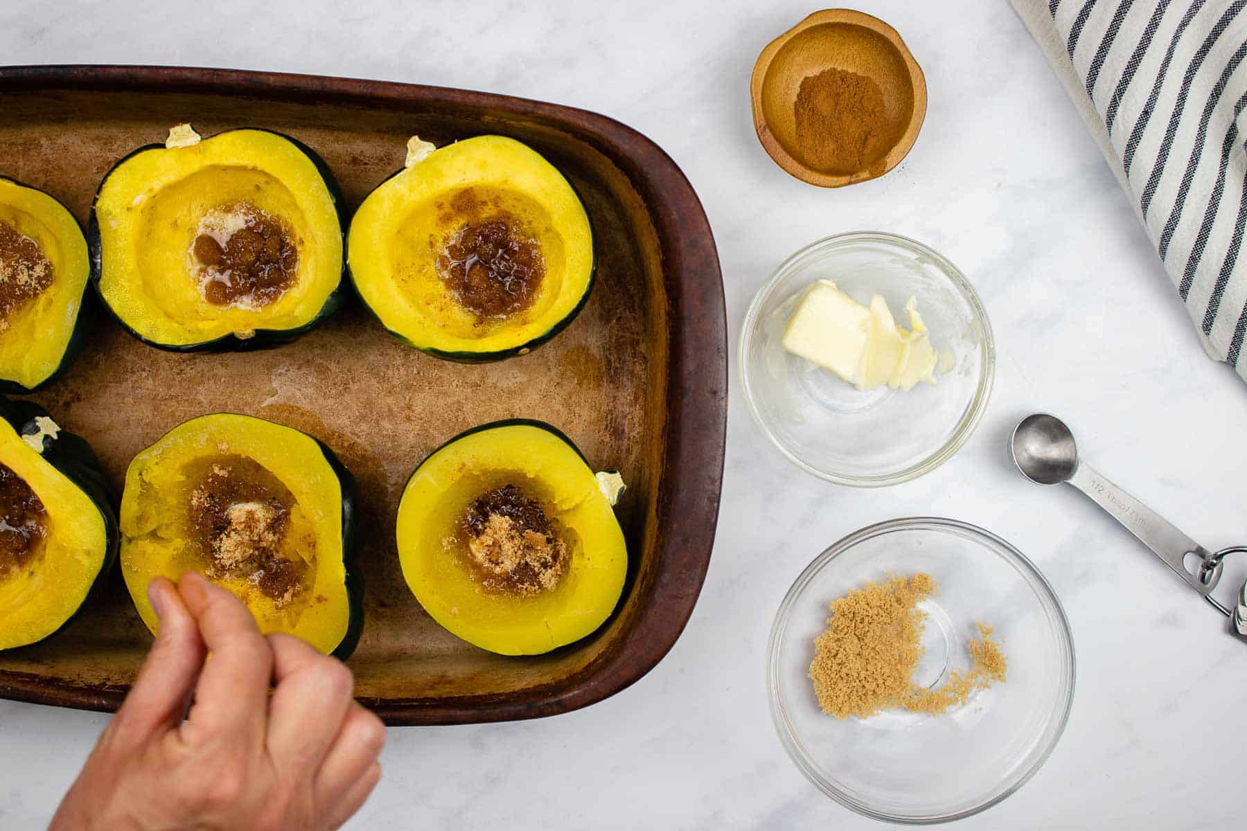 Adding cinnamon to cooked acorn squash halves with butter and brown sugar.