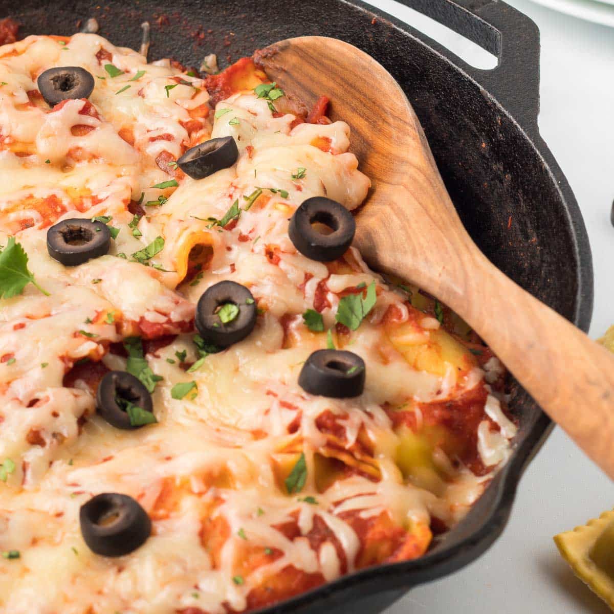 Mexican Ravioli Cast iron skillet with cooked ravioli mixed with salsa, herbs, and tomato sauce and topped with cheese, black olives, and cilantro.