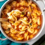 Ladleful of Tomato Zucchini Soup with tortellini over a pot.
