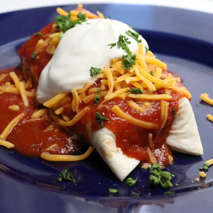 Burrito mojado topped with shredded cheddar, sour cream, and chopped cilantro.