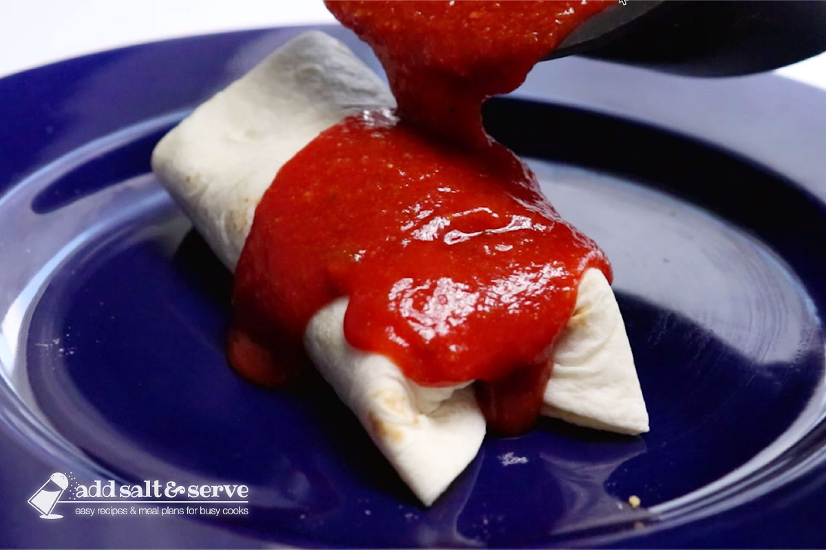 A burrito on a plate with mojado sauce being poured over it.