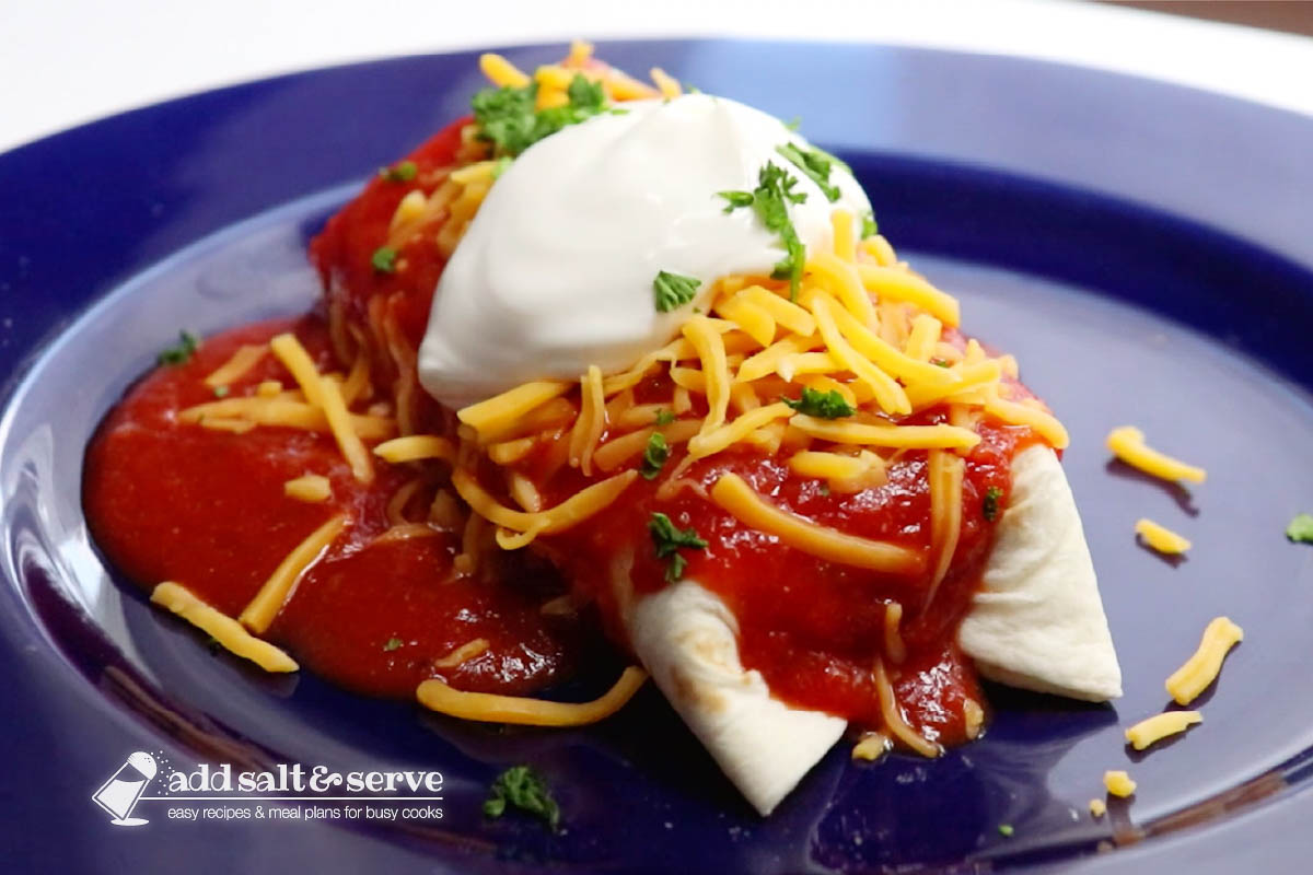 Burrito mojado topped with shredded cheddar, sour cream, and chopped cilantro.