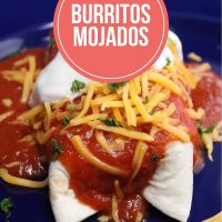 Burrito mojado topped with shredded cheddar, sour cream, and chopped cilantro.