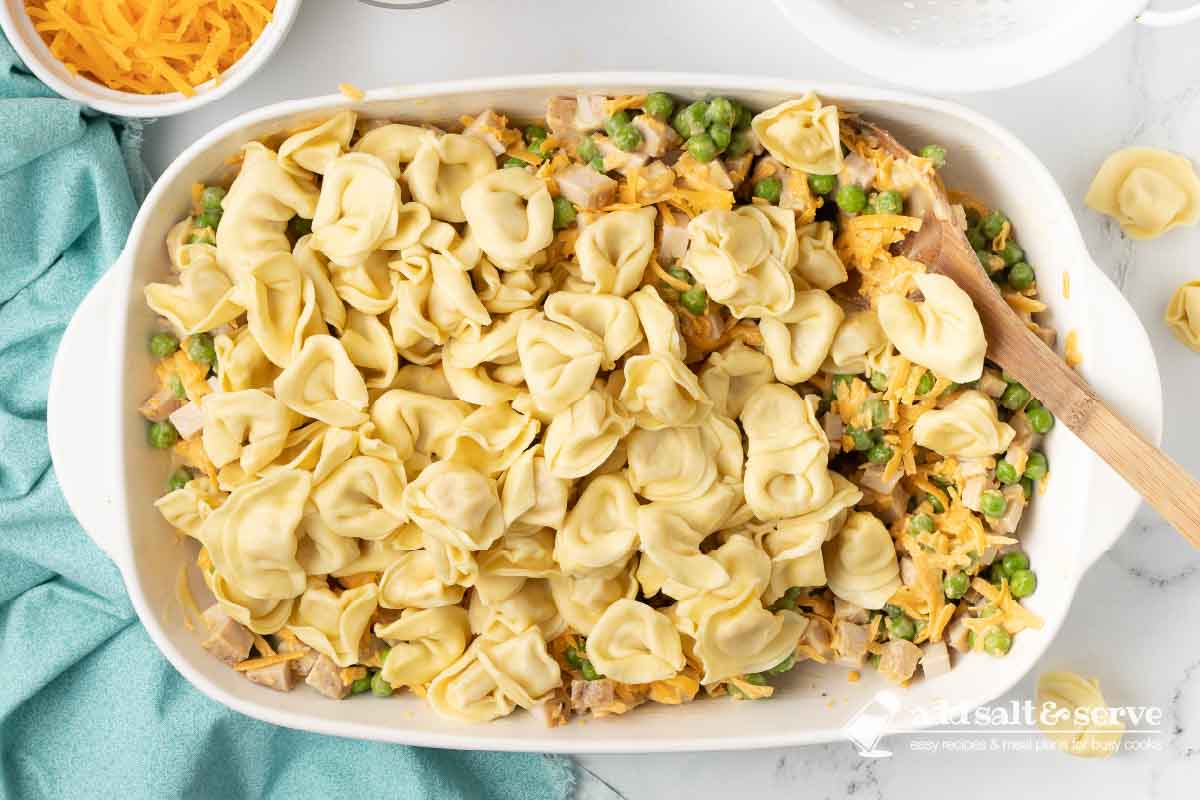 Cooked tortellini added to a casserole dish containing leftover chopped turkey, peas, and a cheese sauce.