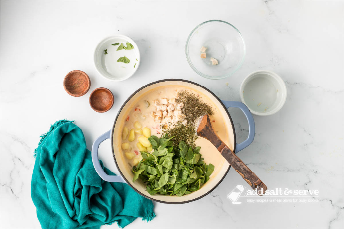 Enamel Dutch oven with Olive Garden Copycat Chicken Gnocchi Soup base with gnocchi, cooked chicken, chopped spinach, and herbs added.