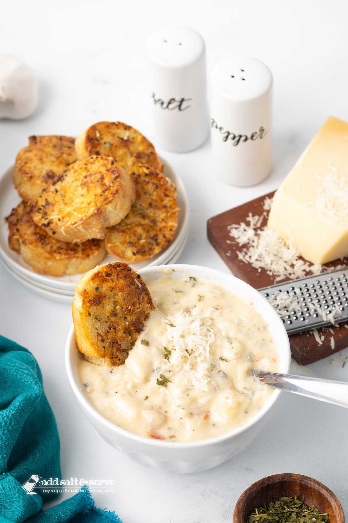 A bowl of Copycat Olive Garden Chicken Gnocchi Soup served with a piece of toasted garlic bread and a wedge of Parmesan cheese with a grater to the side.