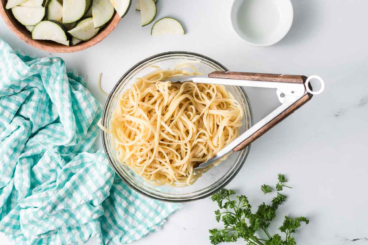 Cooked linguine in a bowl with a bowl of sliced zucchini nearby.