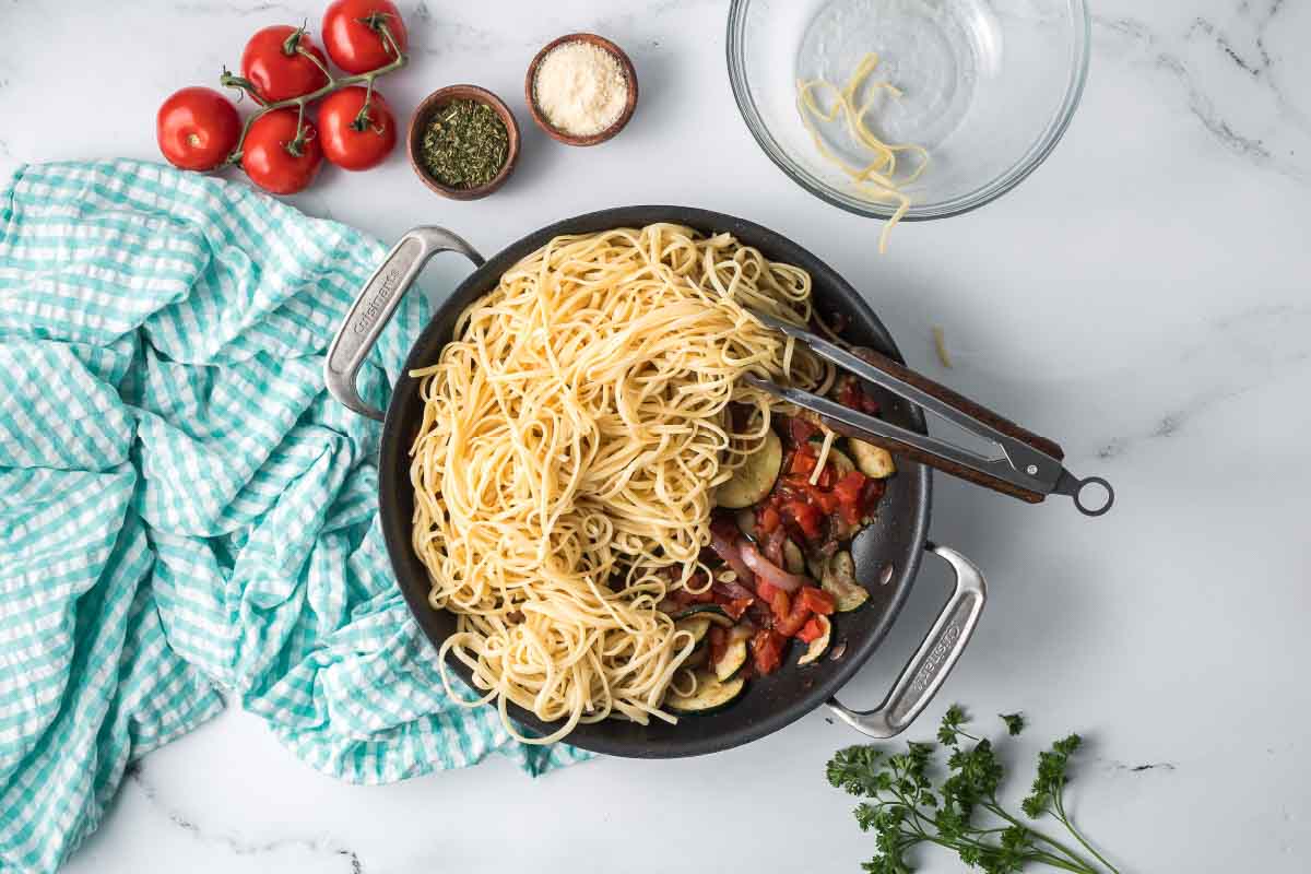 Hot cooked linguine added to a skillet with canned diced tomatoes, sautéd red onion and zucchini, garlic, and herbs.