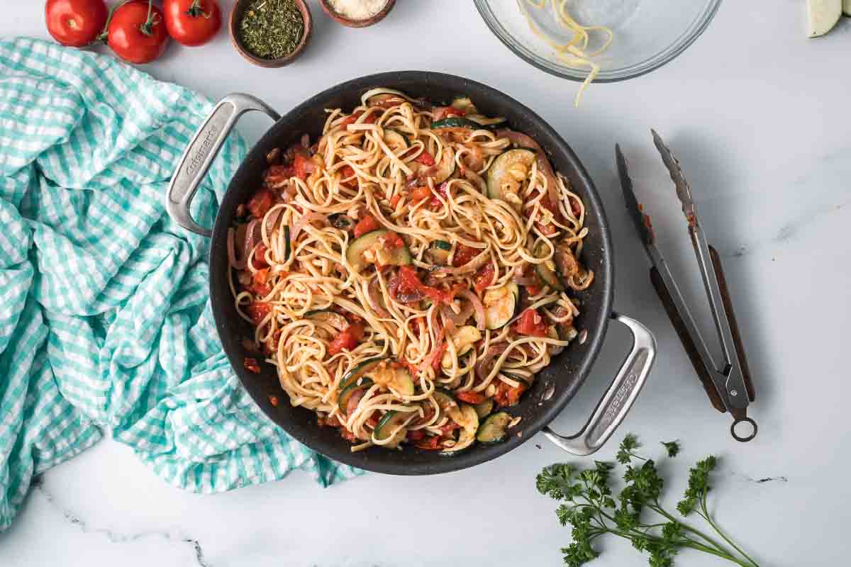 Cooked zucchini linguine consisting of linguine with tomatoes, garlic, zucchini, onion, and herbs in a skillet.