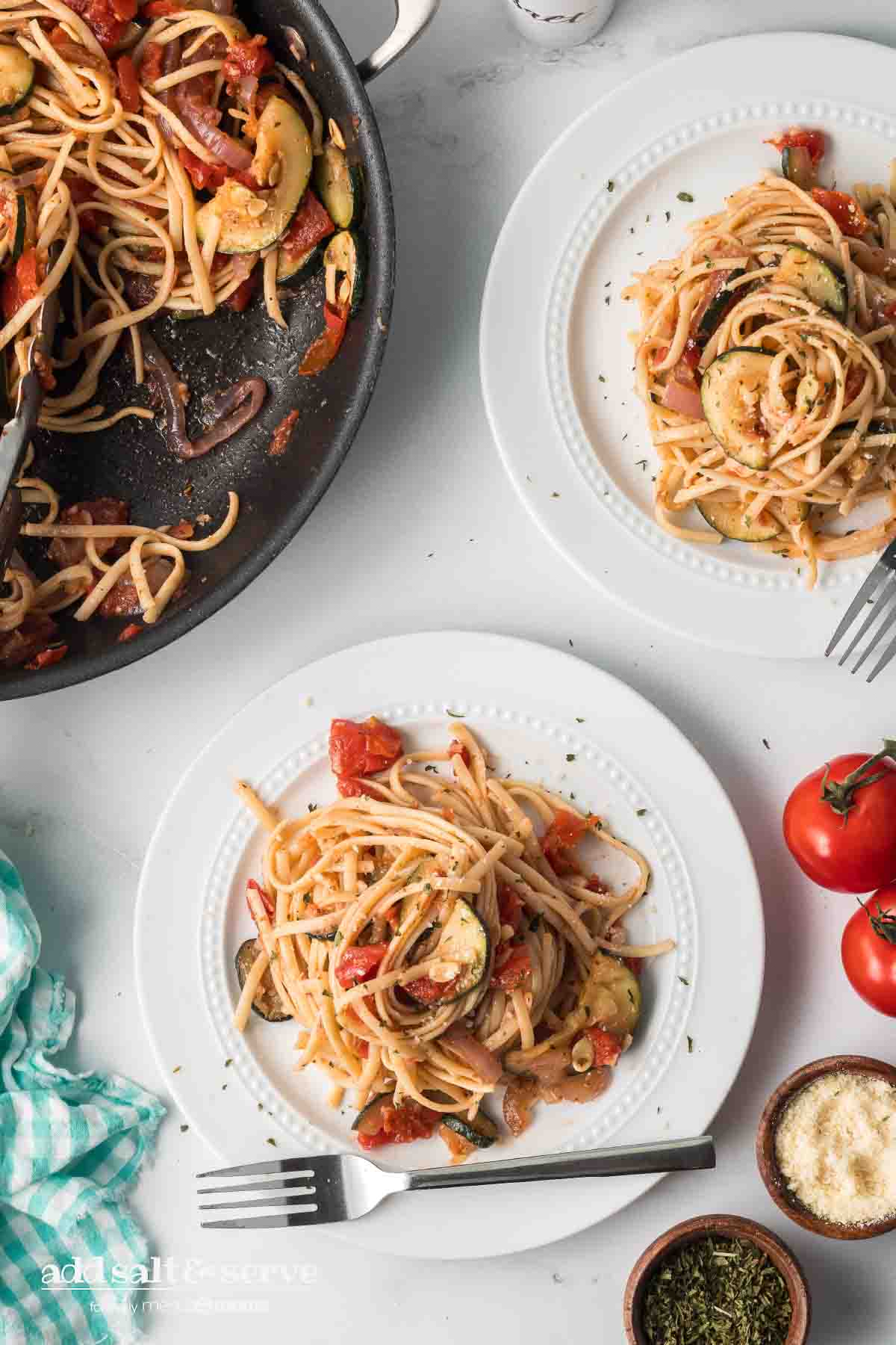 Linguine with tomatoes, garlic, zucchini, onion, and herbs on a plate with skillet of remaining zucchini linguine recipe.