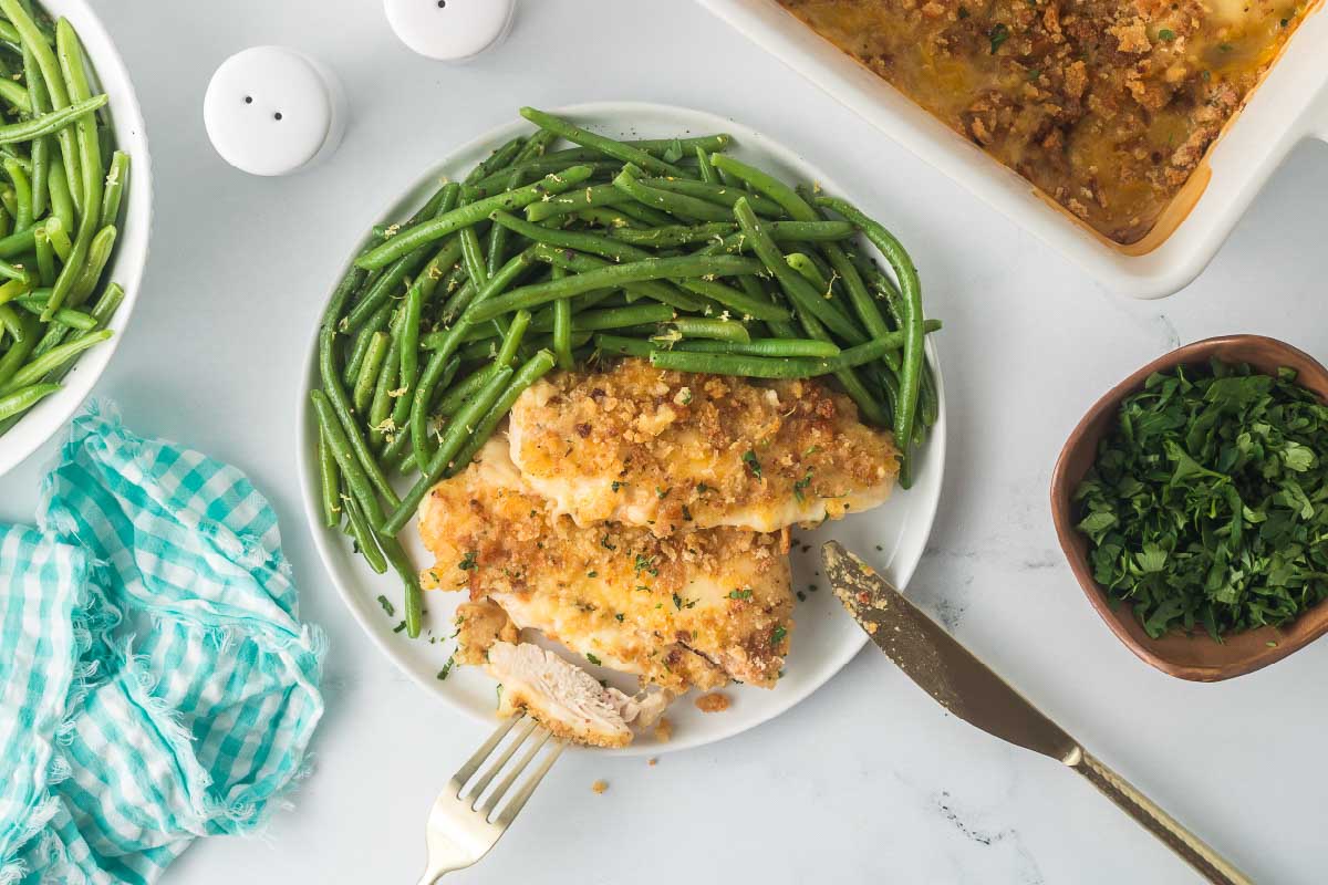 Baked Swiss Chicken plated with seasoned green beans and a forkful of Swiss chicken propped on the plate.