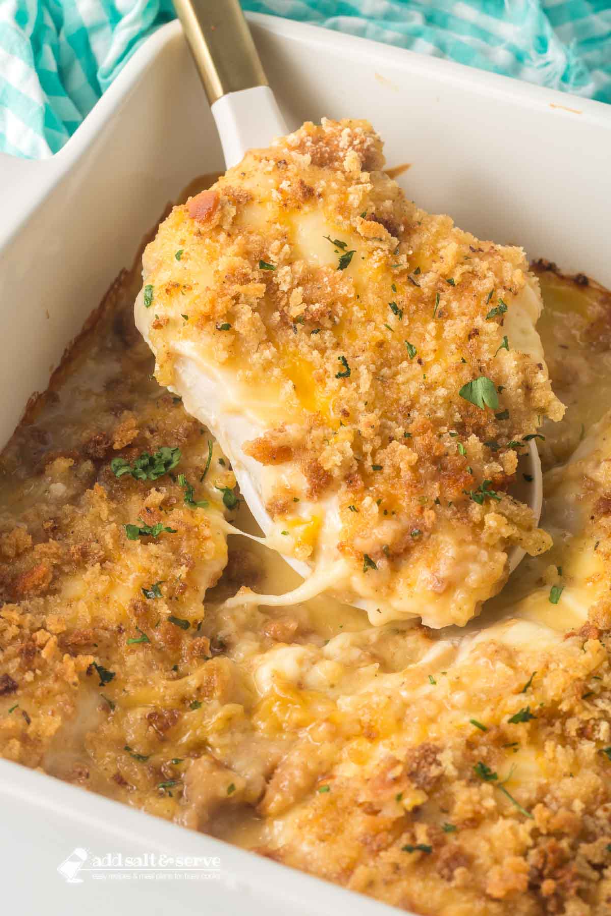 Swiss chicken with white wine and stuffing in a casserole dish with a serving spoon lifting a serving out.