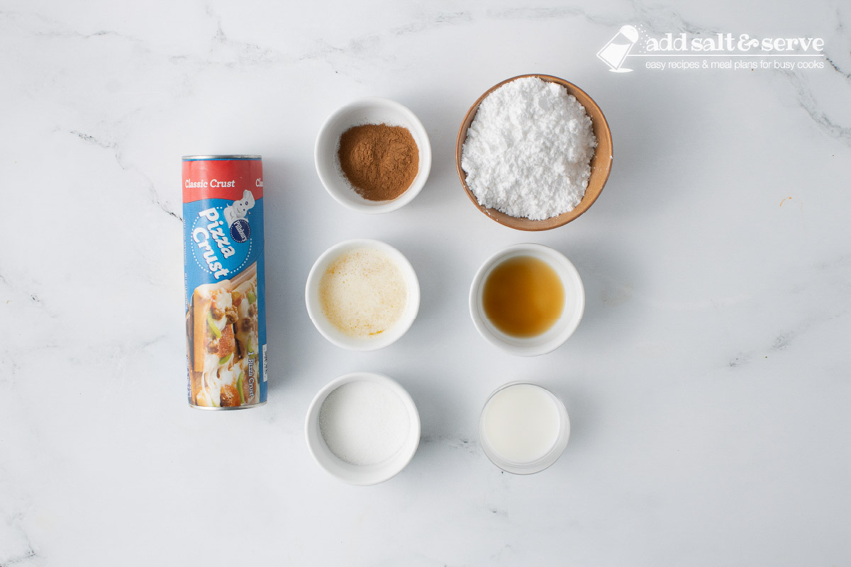Ingredients for cinnamon sticks (pizza crust dough, cinnamon, sugar, butter, vanilla, milk, powdered sugar).