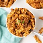 Spiral pasta bake with cheese and ground beef served in white bowls.