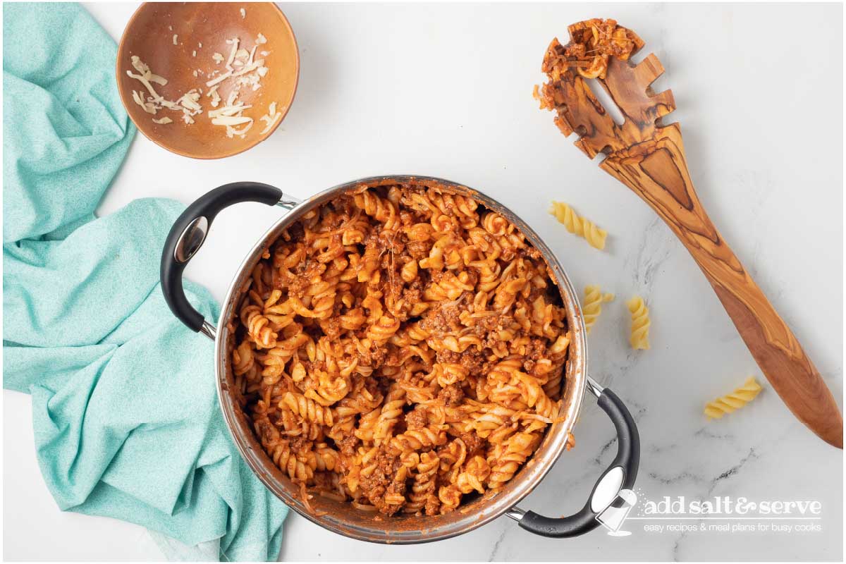 Large pot with spiral pasta with cheese and ground beef served in white bowls.