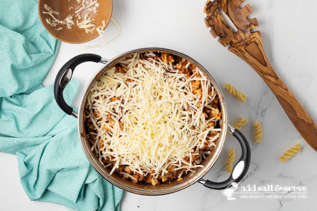 Large pot with spiral pasta recipe mixture with cheese sprinkled on top not yet mixed in.