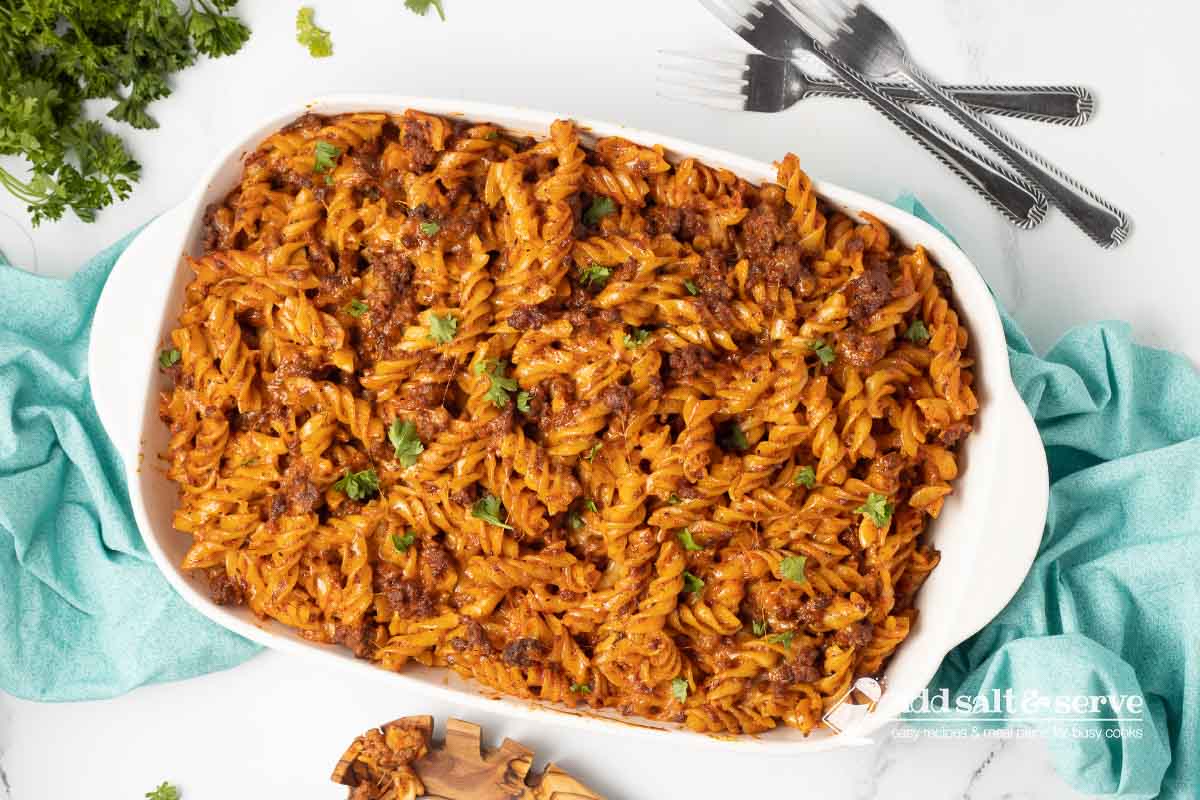 Spiral pasta bake in a white casserole dish garnished with fresh parsley.
