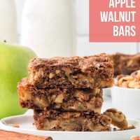 Three Apple Walnut Bars stacked on a white plate with a bowl of walnuts and a green apple in the background.
