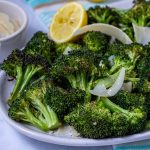 Roasted broccoli florets on a plate, garnished with a lemon half