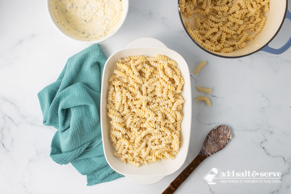 A white baking dish with a layer of rotini and Alfredo sauce mixture spread evenly across the bottom.