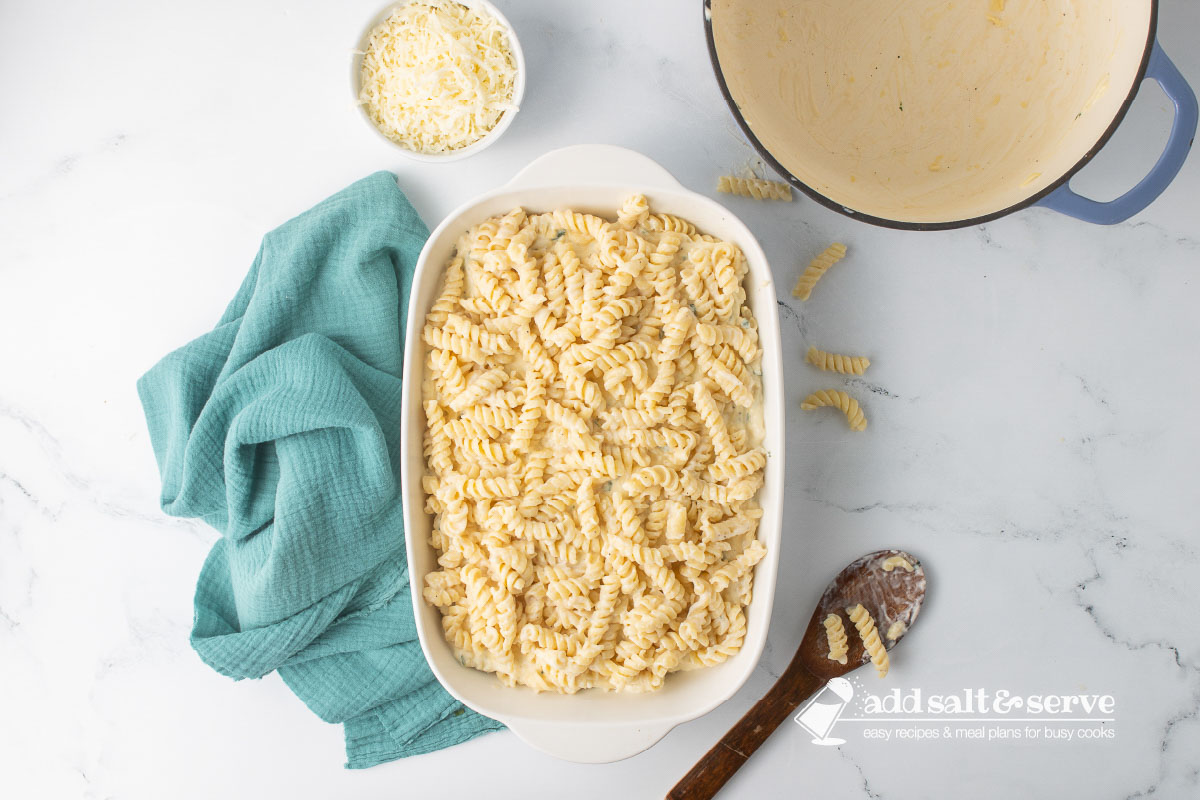 A white baking dish with a layer of rotini and Alfredo sauce, then ricotta cheese and egg mixture, then another layer of rotini and Alfredo sauce.