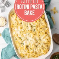 Alfredo Rotini Pasta Bake in a baking dish resting on a tea towel with forks, shredded cheese, and chopped fresh parsley surrounding the pan.