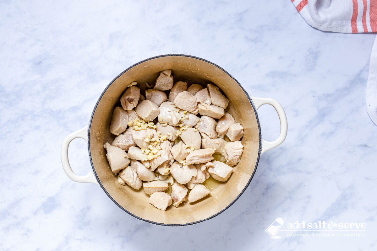 Enameled Dutch oven with sautéed chicken and with minced garlic just added.