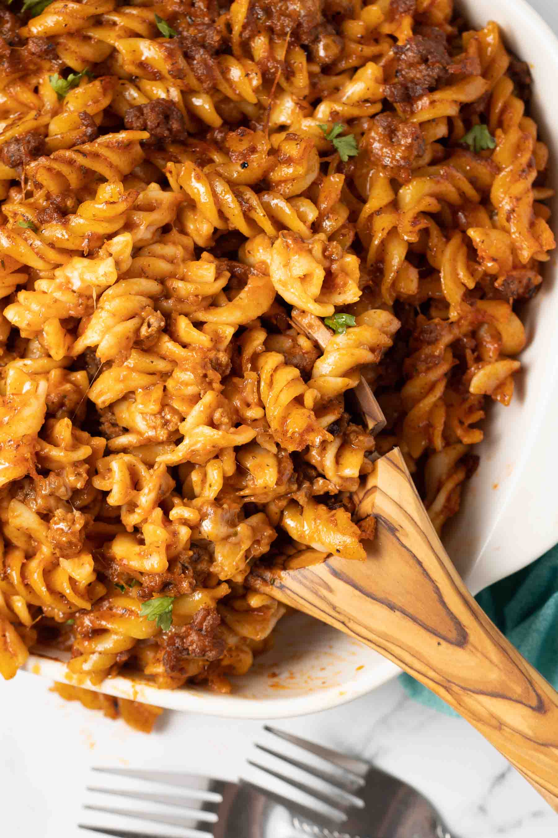 Spiral pasta bake in a white casserole dish with a serving on a wooden spoon in the dish.