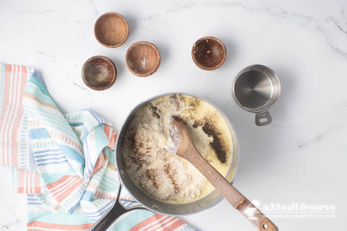 A sauce pan with cream, melted butter, Parmesan cheese, slat, pepper, nutmeg, and minced garlic.