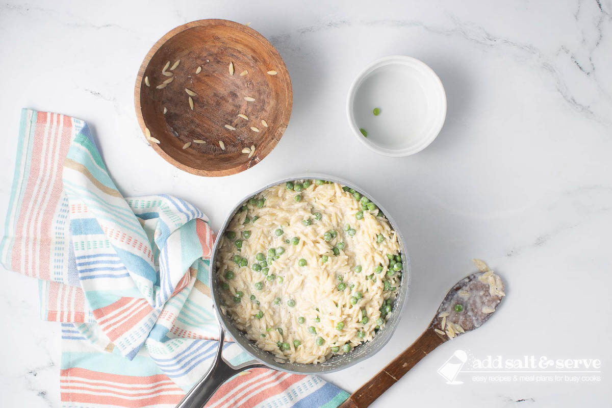 A sauce pan with homemade Alfredo sauce, cooked orzo, and peas after mixing.