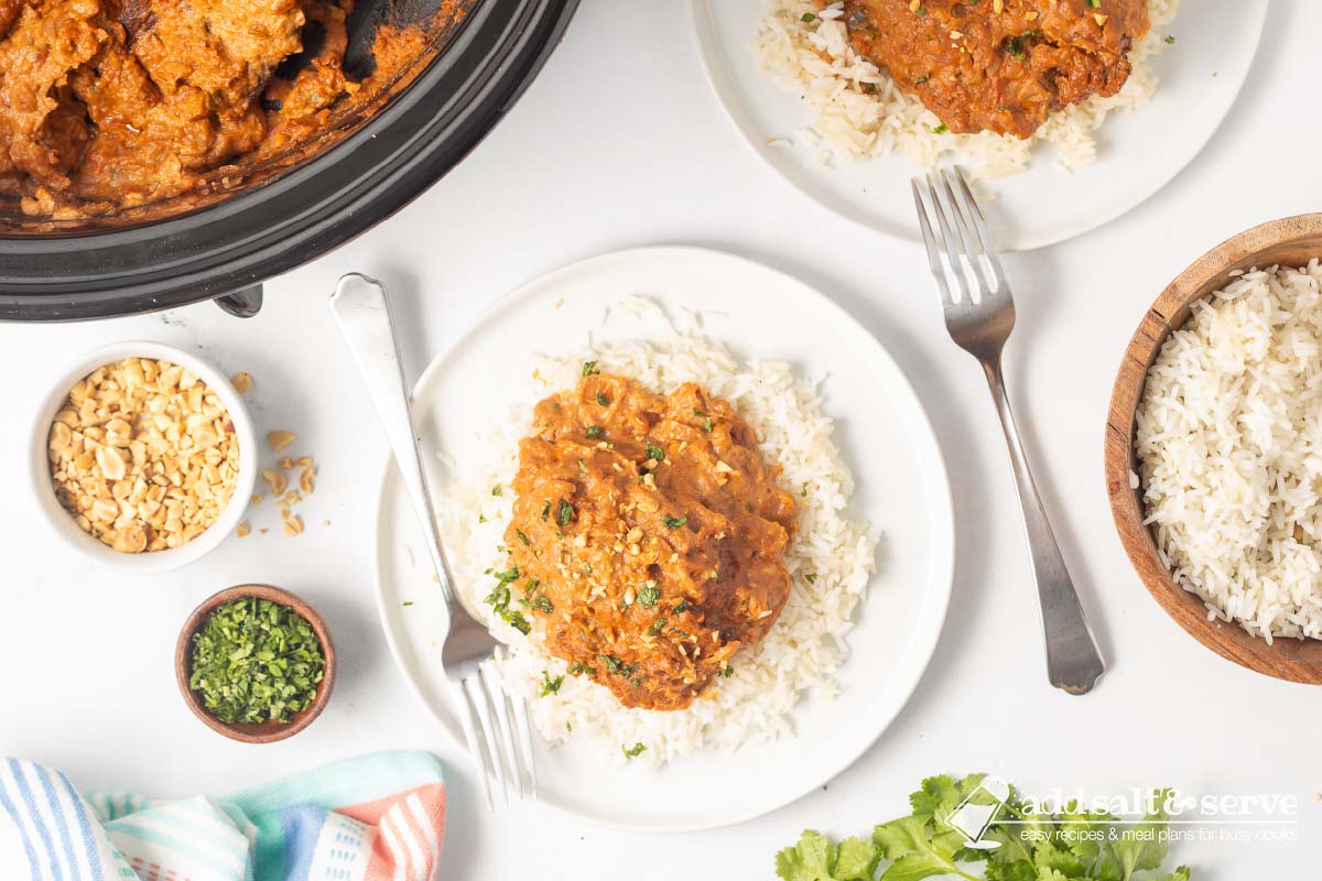 Plated slow cooker Thai Peanut Chicken over rice garnished with chopped peanuts and cilantro.