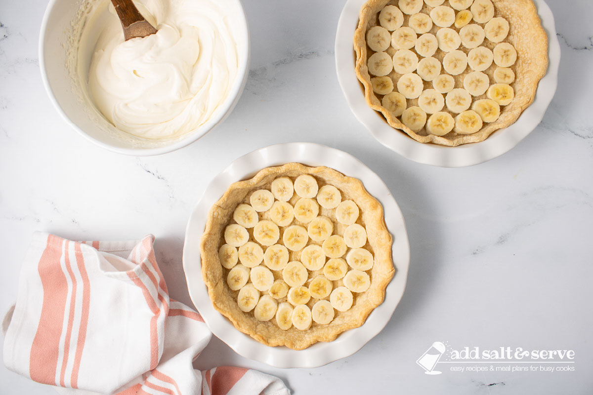 Two pie crusts with sliced bananas layered in the bottoms of the crusts.