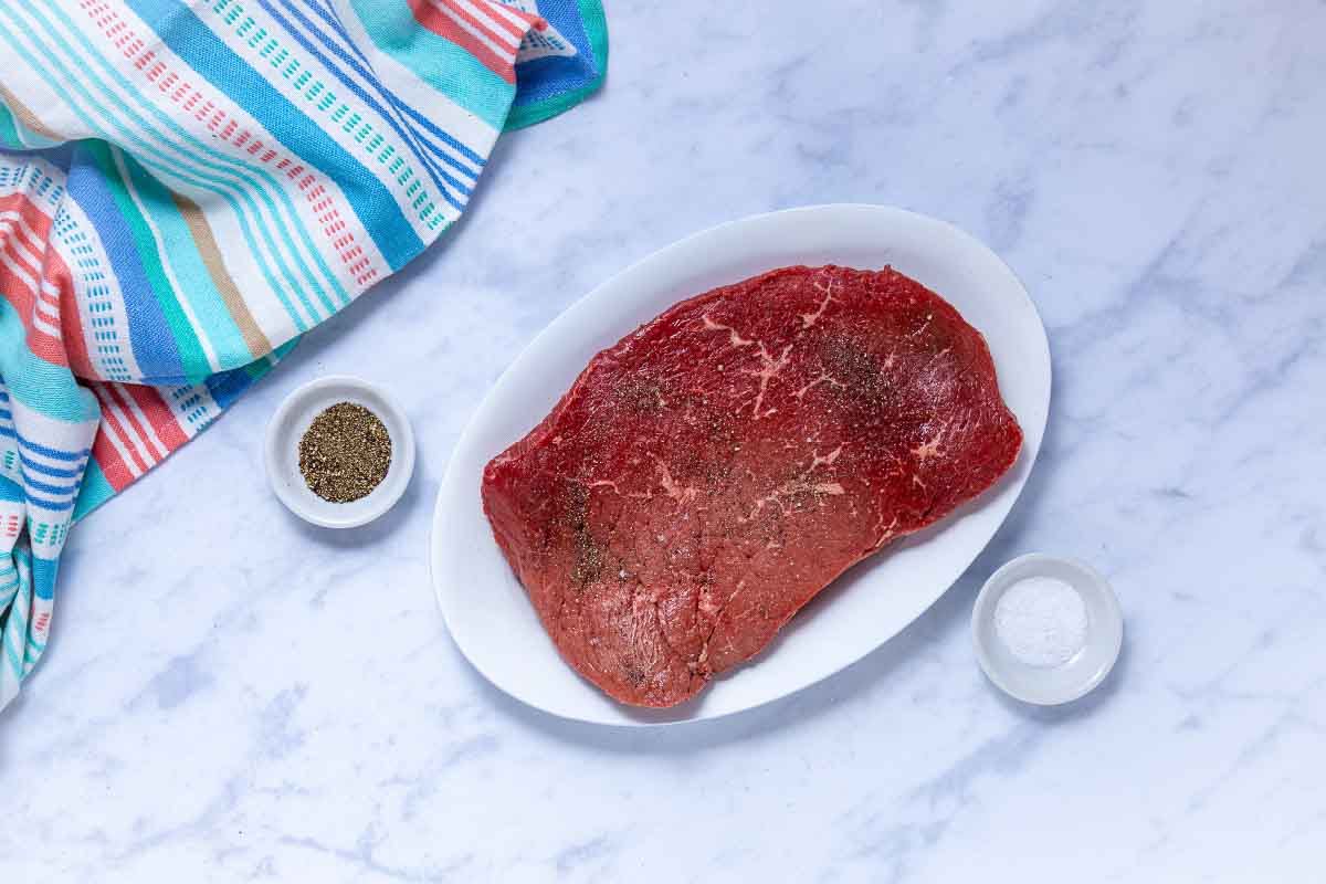 Uncooked London broil roast seasoned with salt and pepper.