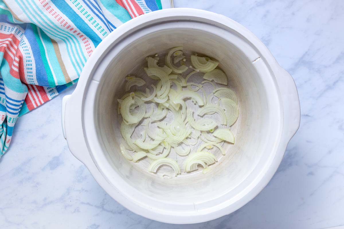 Sliced onions in the bottom of a crock pot.