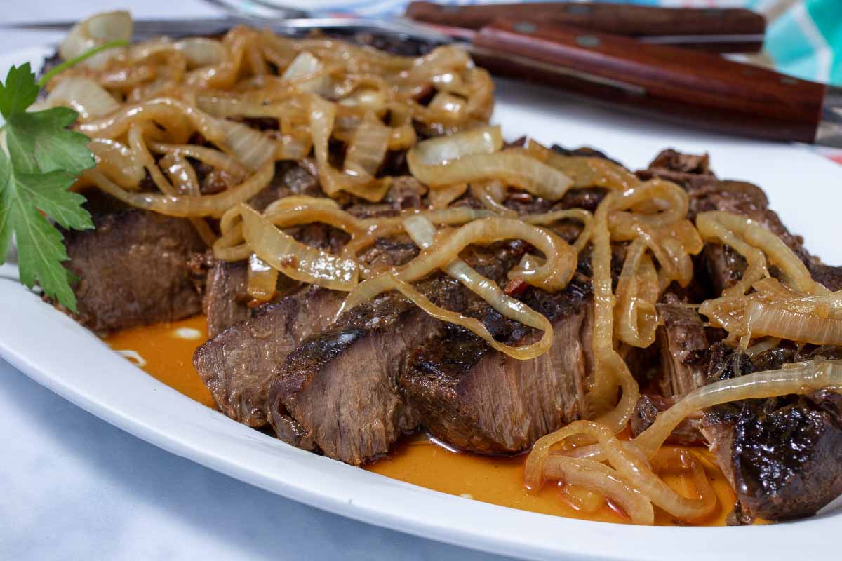 Sliced crock pot London Broil with au jus topped with tender onions.