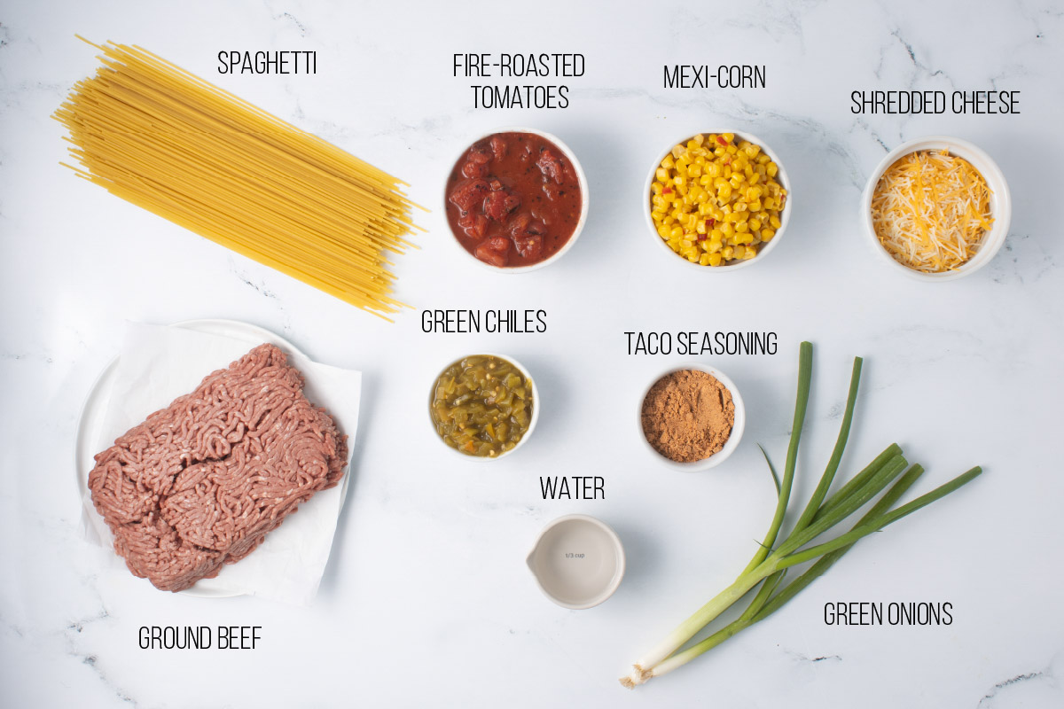 Ingredients for Mexican Spaghetti: dry spaghetti, ground beef, green chiles, green onion, mexi-corn, fire-roasted tomatoes, water, taco seasoning, green onions, and shredded cheese