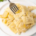 Plate of creamy summer squash and cheese ravioli in a cheese sauce with a forkful lifted to the camera.