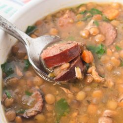 Bowl of lentil soup with kielbasa, spinach, carrots, onion, and green pepper with a spoonful held above the bowl.
